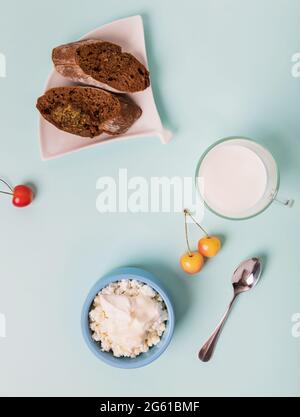 Ricotta il formaggio in una ciotola blu con panna acida e miele. Tostare il pane in un piatto. Colazione del mattino. Foto Stock