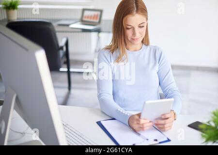 La giovane donna ha girato con un'angolazione elevata utilizzando un tablet digitale e facendo dei documenti in ufficio. Foto Stock