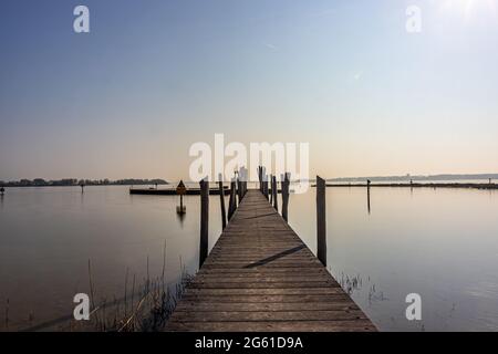 Ponte dritto in legno tra acque calme verso l'area ricreativa dell'Atollo presso la spiaggia di Woldstrand Zeewolde, tramonto in una giornata di primavera a Flevoland, Foto Stock