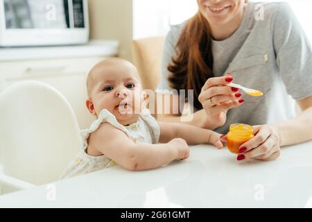 La faccia di un bambino soddisfatto che mangia purea vegetale da un cucchiaio, la mamma alimenta il bambino. Foto Stock