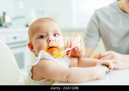 Primo piano del viso di un bambino macchiato con purea di verdure. La mamma alimenta il bambino. Foto Stock