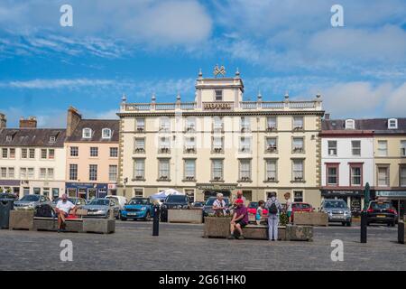 Persone che siedono nella piazza di Kelso con il Cross Keys Hotel sullo sfondo, Scottish Borders, Scozia, Regno Unito Foto Stock