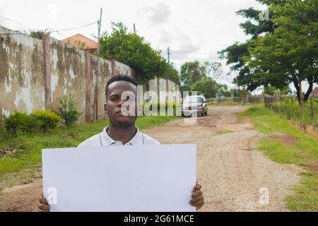 Primo piano di un maschio africano della Nigeria che tiene un poster vuoto su una strada rurale Foto Stock