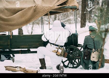 Il Re-enactor nascosto vestito come soldato tedesco della fanteria Wehrmacht nel mondo Guerra II soldati seduti in Ambush vicino Peasant Cart in Foresta invernale e. Foto Stock