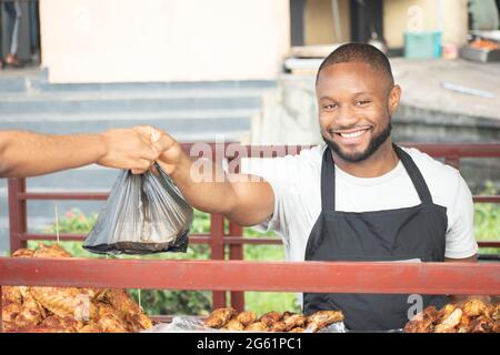uomo africano che serve pollo alla griglia da take out Foto Stock