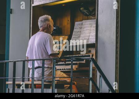 Un vecchio si siede davanti alle note e suona l'organo Foto Stock