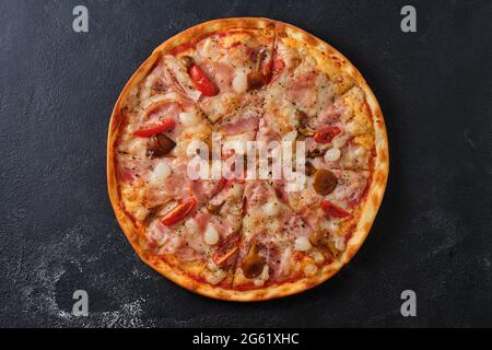 Pizza con pomodori, pancetta, cipolle sottaceto, funghi al miele, mozzarella, spezie e salsa di pomodoro. Disposizione piatta. Su sfondo scuro. Foto Stock