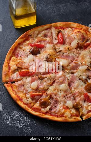 Pizza con pomodori, pancetta, cipolle sottaceto, funghi al miele, mozzarella, spezie e salsa di pomodoro. Su sfondo scuro. Foto Stock
