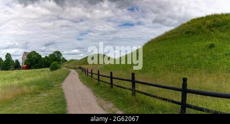 pittoresco paesaggio rurale con un sentiero in ghiaia lungo colline erbose e una lunga recinzione di legno marrone Foto Stock