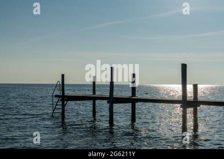 Caldo tramonto sull'oceano con un molo in legno e una scala per nuotare in primo piano Foto Stock