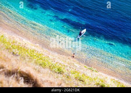 Donna che entra in mare e uomo su una tavola da paddle a Man o'War Beach a Dorset, Jurassic Coast, Regno Unito Foto Stock