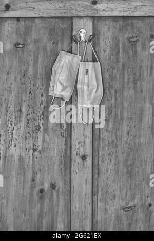 Grinty black & white abstract of his and Hers facemasks appeso alla vecchia porta. Per Covid UK, non indossare maschere facciali, American mask mandato, rimanere a casa Foto Stock