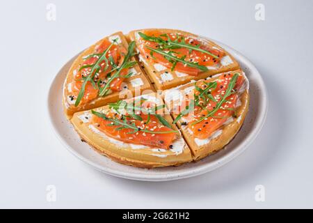 Waffle belgi salati per colazione su un piatto bianco. Waffle con salmone, formaggio spalmabile, rucola e semi di sesamo. Foto Stock