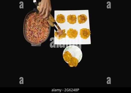 Dettaglio della degustazione di alcuni Totteri con insalata di carote grattugiate, cavolo, lattuga, maionese. I Patacones sono tipici della gastronomia caraibica Foto Stock