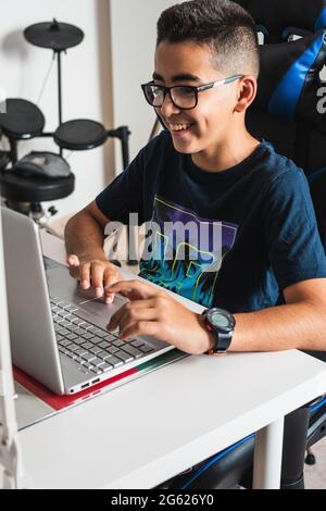 Il caucasico pre-teen gioca, studi o surfs con il suo laptop sulla sua scrivania nella sua stanza, Foto Stock