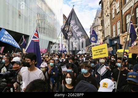 I manifestanti si riuniscono alla Chinatown di Londra durante la dimostrazione. Hongkongers ha tenuto manifestazioni in dieci diverse città del Regno Unito per protestare contro il primo anniversario della promulgazione della legge sulla sicurezza nazionale di Hong Kong e il centenario del Partito comunista cinese. A Londra, i partecipanti si sono riuniti fuori dall'ambasciata cinese e hanno marciato verso Chinatown, dove si è svolto l'evento principale. Le folle poi si trasferirono all'Hong Kong Economic and Trade Office e rimassero le zampate di fumo all'esterno come un segno simbolico di maledizione del governo di Hong Kong. Foto Stock