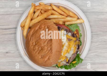 Vista dall'alto di un enorme cheeseburger che scivola fuori dal panino con un lato generoso di patatine fritte. Foto Stock