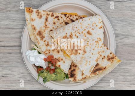 Vista dall'alto della quesadilla alla griglia tagliata in quarti, servita con un generoso cucchiaio di panna acida e guacamole per pranzo. Foto Stock