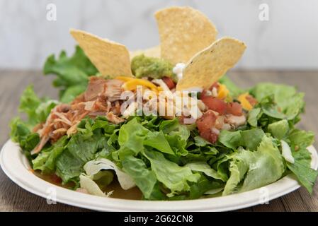 Insalata di Taco accatastata sul piatto pieno di lattuga, asada di carne, patatine, e panna acida per un pasto delizioso. Foto Stock