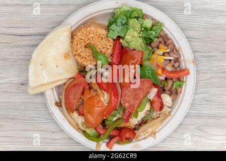 Vista dall'alto della fajitas di pollo, calda dalla griglia accatastata con verdure e grandi pezzi di carne su un piatto con tortillas. Foto Stock