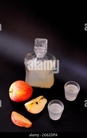 Due bicchieri e un decanter di vetro del Calvados, accanto ad esso sono fette di mela matura su uno sfondo nero. Primo piano. Foto Stock