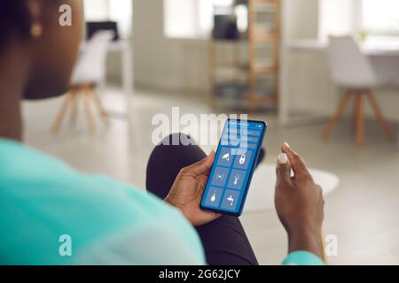 Black Woman controlla il sistema della sua Smart House utilizzando un'app sul suo telefono cellulare Foto Stock