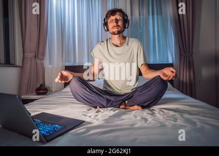 L'uomo medita a letto utilizzando l'app di meditazione. Sport, tecnologia e stile di vita sano Foto Stock