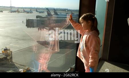 Bambina che guarda l'aereo parcheggiato all'aeroporto di Mosca attraverso la finestra del cancello. Manutenzione e preparazione dell'aeromobile per il reggimento Foto Stock