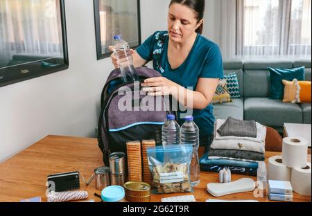 Donna che mette una bottiglia d'acqua per preparare lo zaino di emergenza Foto Stock