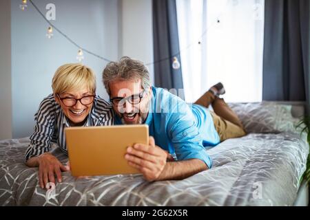 Felice coppia matura sorridente che usa il tablet digitale a casa Foto Stock