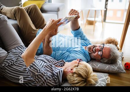 Bella coppia sorridente matura che si diverte mentre si usa tablet a. casa Foto Stock
