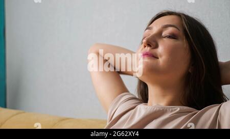 donna che si gode il vento dal ventilatore mentre si siede sul divano, primo piano. Foto Stock