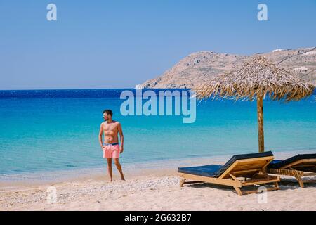 Elia Beach Mykonos, un giovane ragazzo sulla spiaggia di Mykonos durante l'estate con un ombrellone e sedie da spiaggia di lusso letti, l'oceano blu a Elia spiaggia Mykonos Grecia. Foto Stock