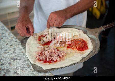 Il pizzaiolo mette sulla buccia una pizza di quattro stagioni, pronta per la cottura. Foto Stock