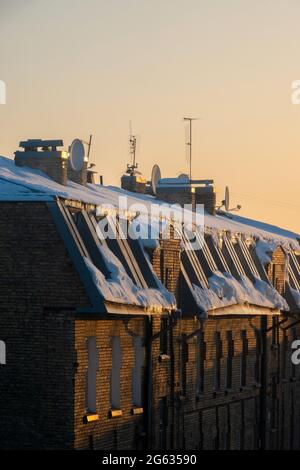 TV e antenne via cavo sul tetto di una casa di appartamenti coperta di neve al tramonto. Foto Stock