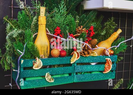 Decorazioni natalizie appese a parete. Rami di abete, coni, arance secche, giocattoli e bottiglie dipinte in scatola di legno Foto Stock