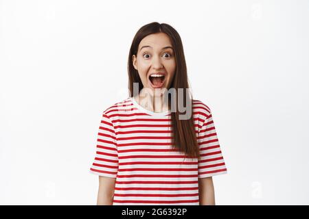 Immagine di ragazza entusiasta sorpresa caduta mascella, gridare da stupore e guardando la macchina fotografica stupito, fissando in stupore a sorpresa per lei, in piedi a strisce Foto Stock