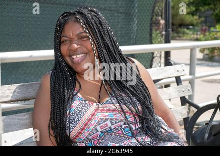 Ritratto di una allegra e ridente bella donna nigeriana americana con lunghe estensioni dei capelli. A Brighton Beach, Brooklyn, New York City. Foto Stock