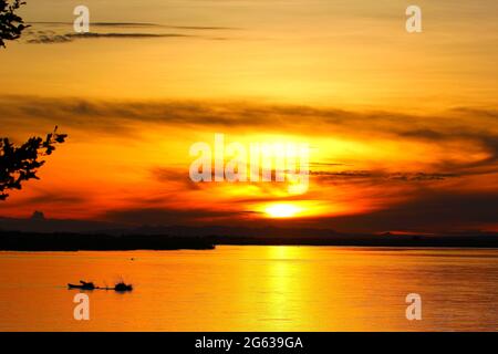 Il sole dorato si tuffa sotto la linea dell'orizzonte illuminando sia il cielo che l'acqua in un'area luminosa di luce arancione. VARIE: Fotografie SBALORDITIVE h Foto Stock