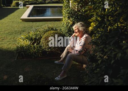 Felice donna caucasica anziana seduta e sorridente in giardino soleggiato Foto Stock