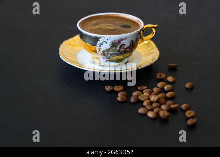 Caffè di moka turco schiumoso su sfondo nero, in una tazza tradizionale gialla, chicchi di caffè in primo piano, Copy Space. Foto Stock