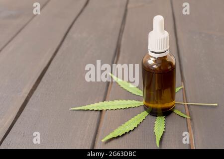 Bottiglia di vetro con dosaggio di gocce di erbe medicina organica olio CBD concentrato su sfondo di legno con foglia verde di marijuana, spazio di copia Foto Stock