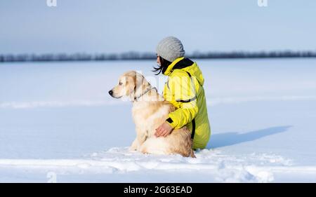 Vista posteriore del cane e della donna amichevoli seduti sulla neve campo Foto Stock