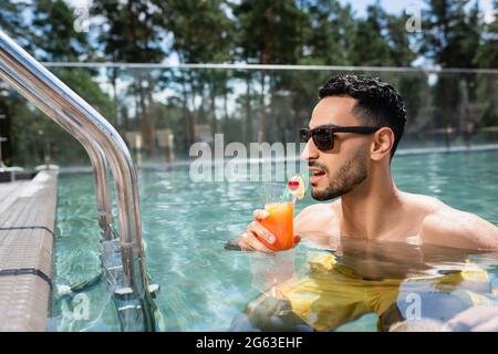 giovane musulmano in occhiali da sole che beve cocktail in piscina Foto Stock