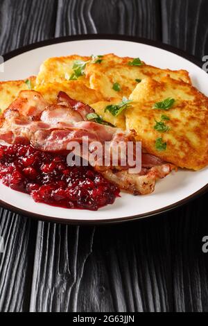 Cibo svedese frittelle di patate con confettura di mirtilli e pancetta primo piano in un piatto sul tavolo. Verticale Foto Stock