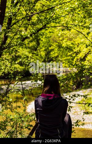 La ragazza si siede sul bordo e guarda il fiume Foto Stock