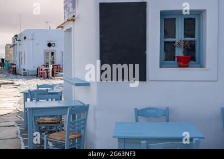 Bar e taverna all'aperto tradizionale. Grecia, porto vecchio di Naousa, villaggio di pescatori greco sull'isola di Paros. Tavoli e sedie vuoti blu, nero Foto Stock