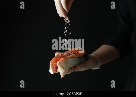 L'uomo spolverò il sale sulla carne di salmone su fondo scuro Foto Stock