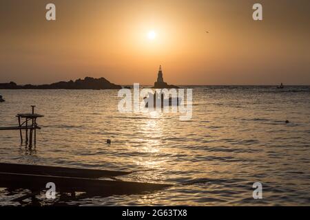 Ahtopol - 10 settembre: Sagoma di una barca con i pescatori di ritorno dalla pesca tra rocce e faro all'alba il 10 settembre 2016, Ahtopol Foto Stock