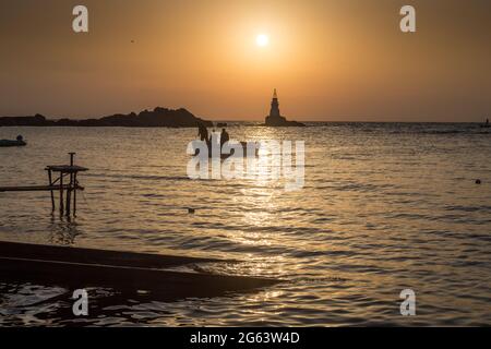 Ahtopol - 10 settembre: Sagoma di una barca con i pescatori di ritorno dalla pesca tra rocce e faro all'alba il 10 settembre 2016, Ahtopol Foto Stock